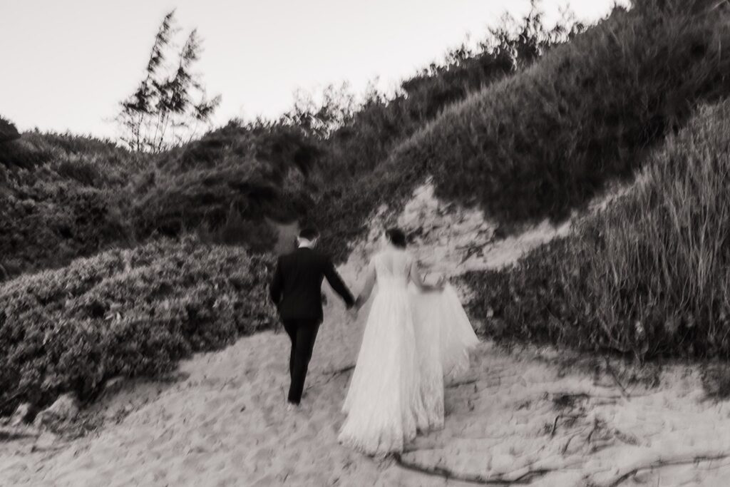 Bride and groom hold hands while walking through the sand at their Kauai wedding