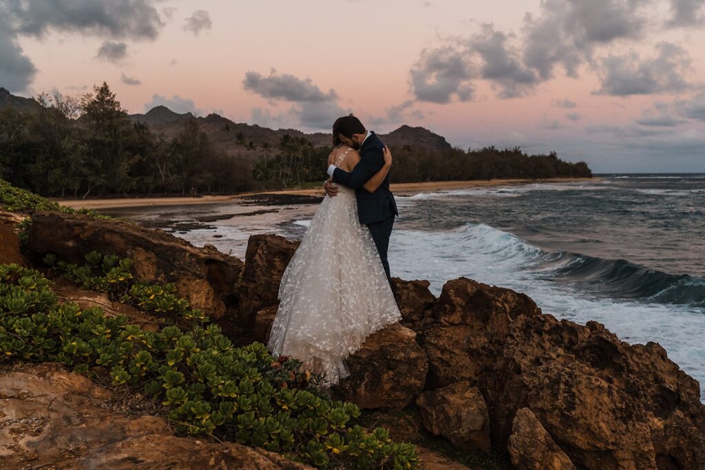Bride and groom hug during sunset photos on the beach in Kauai