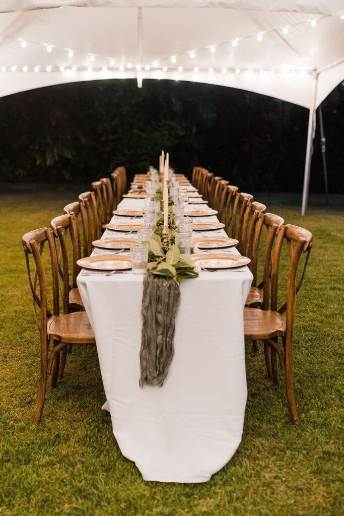 White reception table with wood chairs under a tent with string lights
