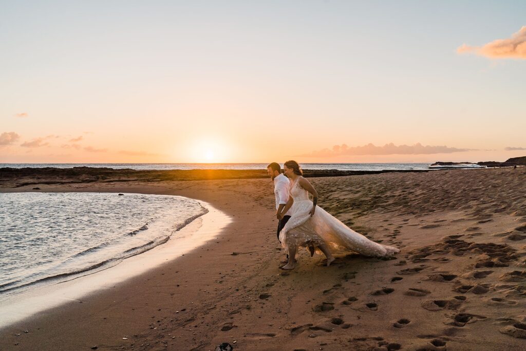 Bride and groom run towards the ocean during sunset photos in Kauai