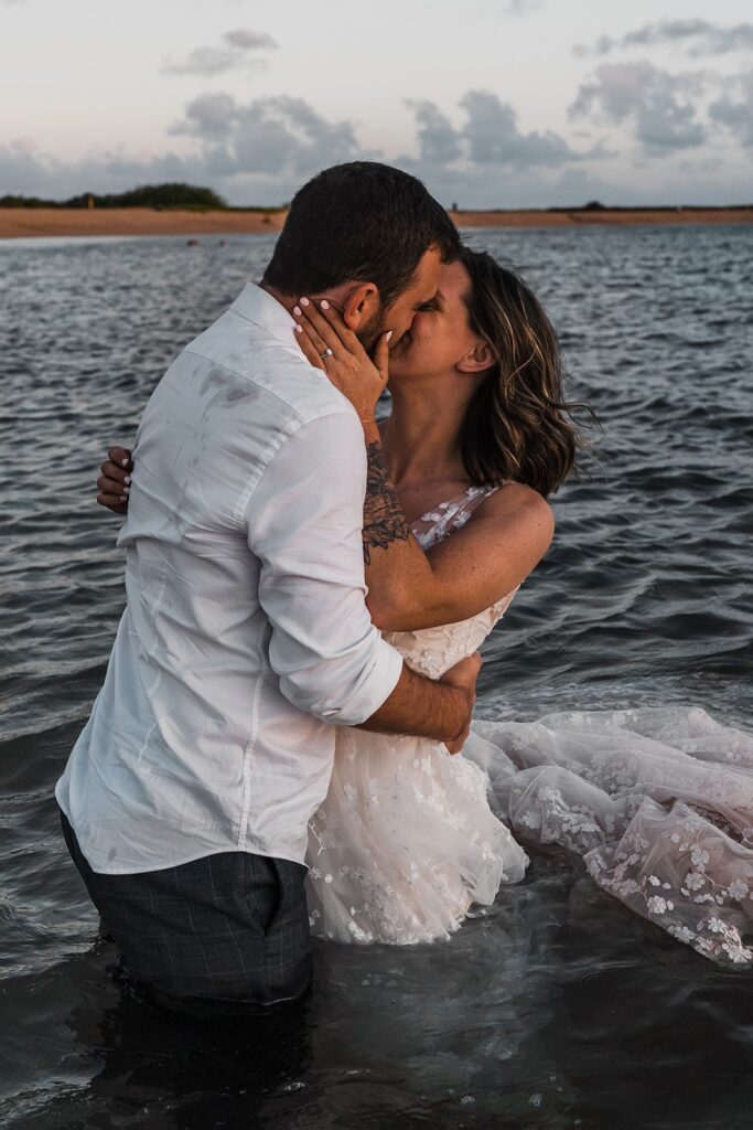 Bride and groom kiss in the ocean during sunset at their two-day wedding on Kauai