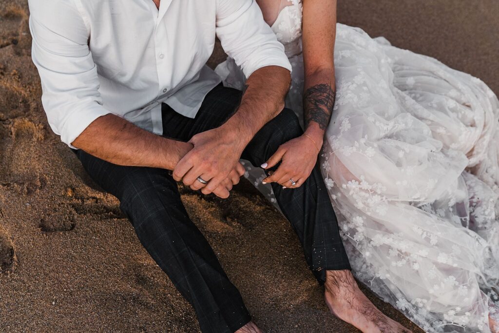 Bride and groom sit in the sand during their sunset photos in Kauai