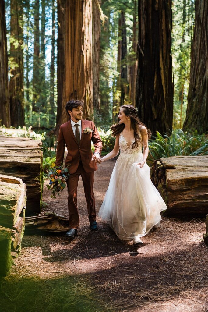 Bride and groom hold hands while walking through the forest during their Redwoods elopement in Oregon