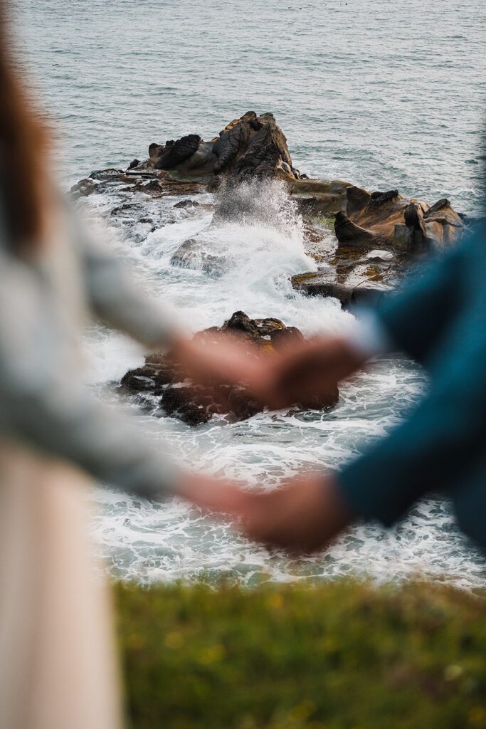 Bride and groom hold hands on a cliff overlooking the ocean during their Oregon Coast elopement at Crook Point