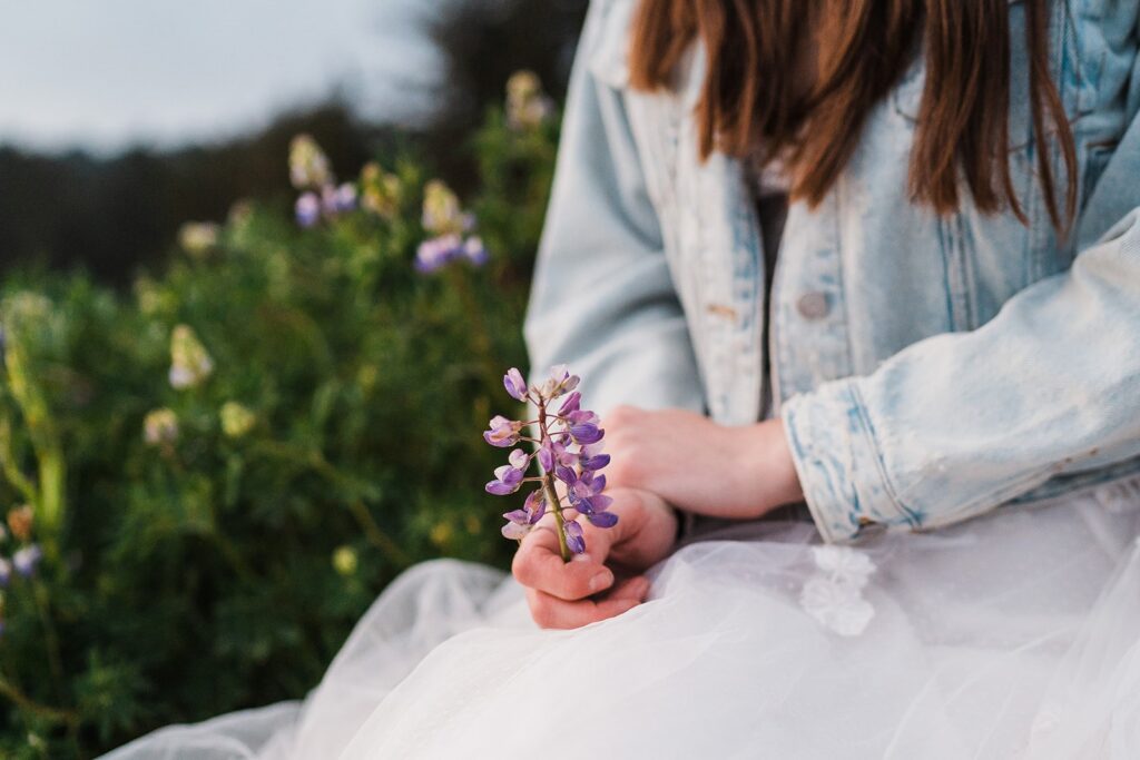 Bride holds purple wildflowers while sitting in the grass during her Oregon Coast elopement