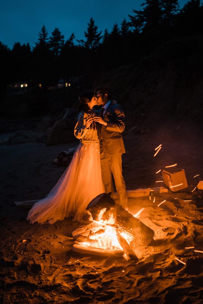 Bride and groom kiss in front of a beach bonfire on the Oregon Coast