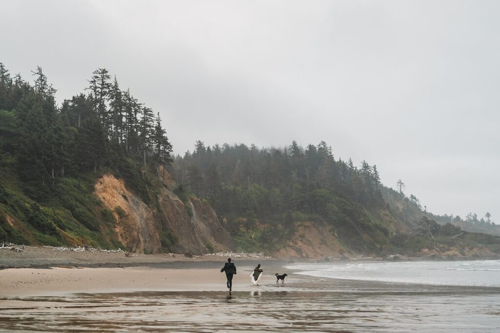 Bride and groom run across the beach with their dog at their Oregon Coast elopement