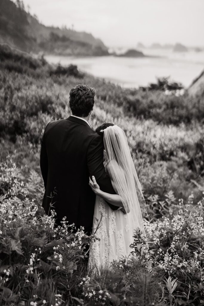 Bride and groom hug while looking out at the ocean during their Oregon Coast elopement