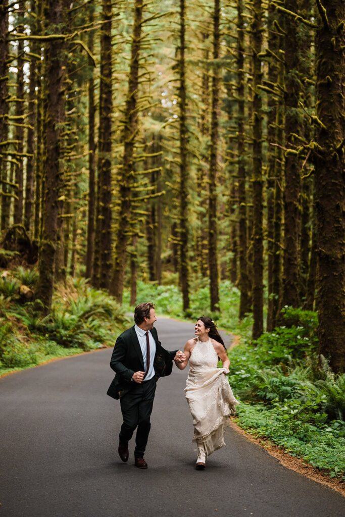 Bride and groom hold hands while running through the road in the forest on the Oregon Coast 