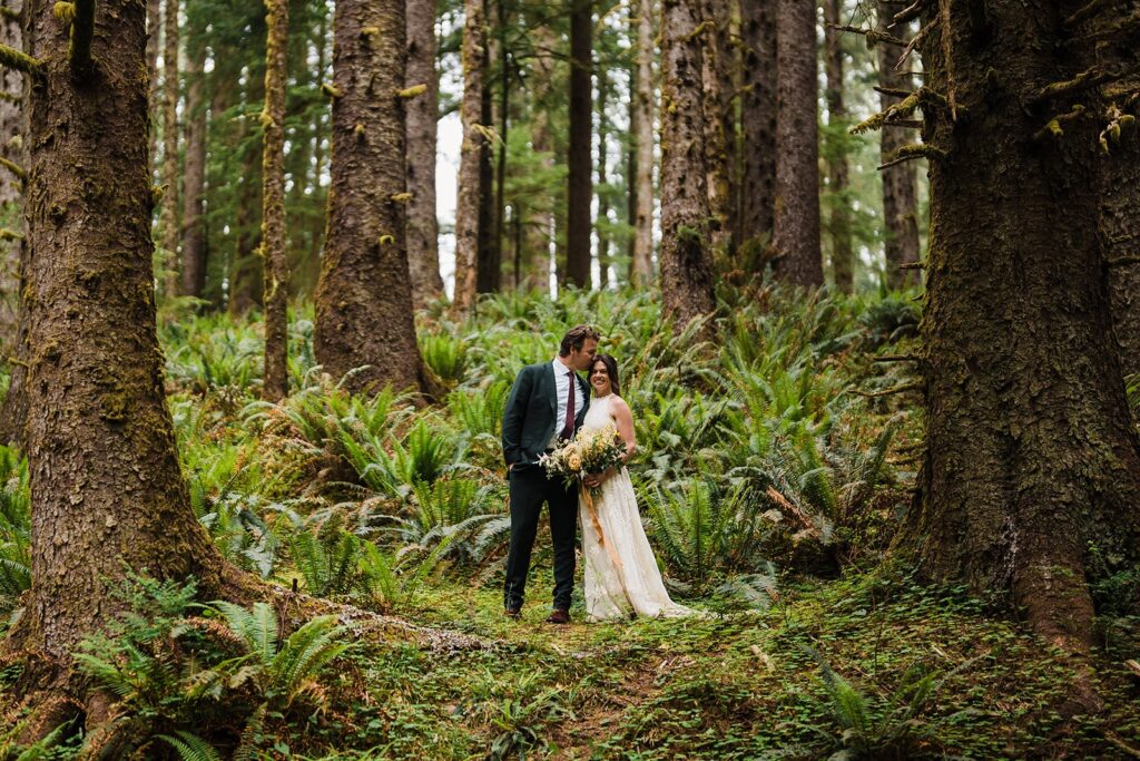 Groom kisses bride on the head during forest elopement photos on the Oregon Coast 