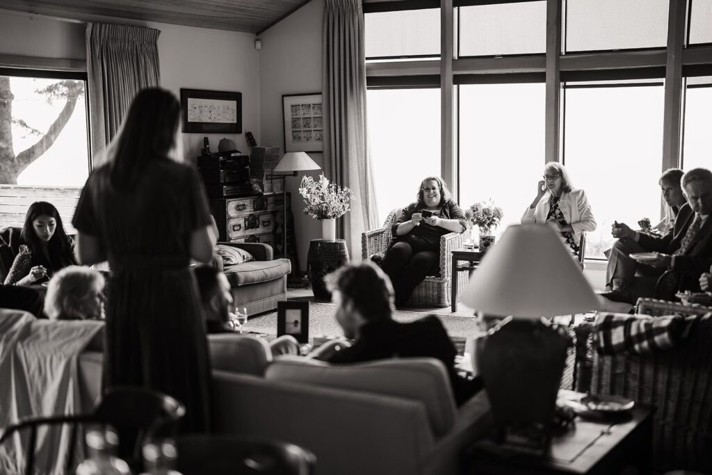 Loved ones sit in the living room of Airbnb cabin giving speeches to the bride and groom after their Oregon Coast elopement