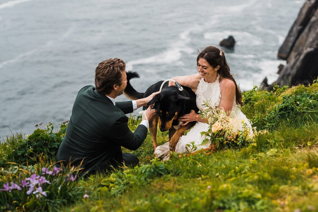 Bride and groom play with their dog while sitting on a cliff overlooking the ocean during their Oregon Coast elopement 