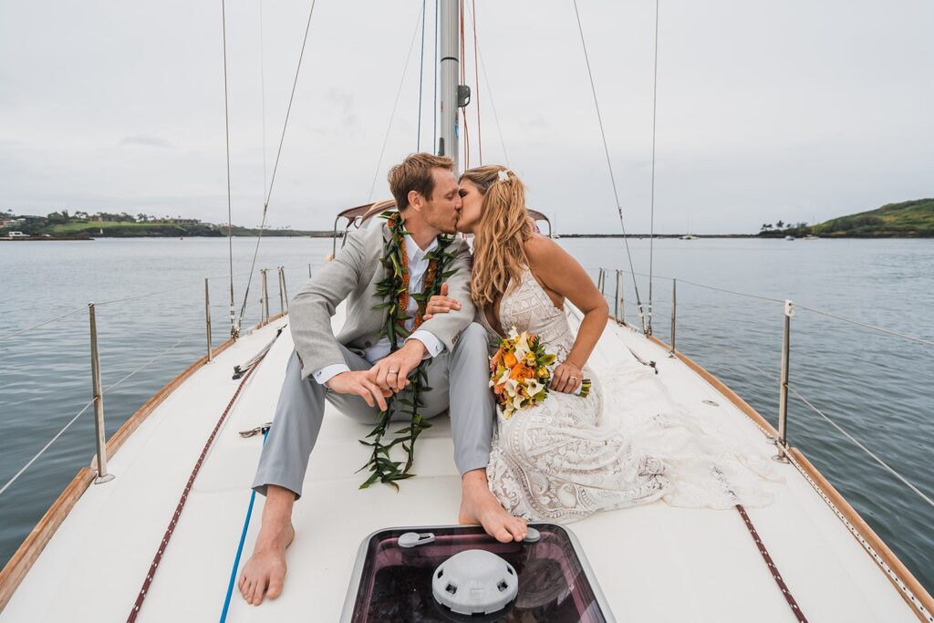 Bride and groom kiss while sitting on a sailboat on the ocean in Hawaii