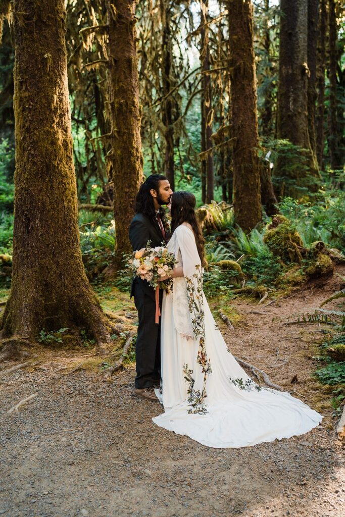 Groom kisses bride on the forehead during elopement photos in the forest