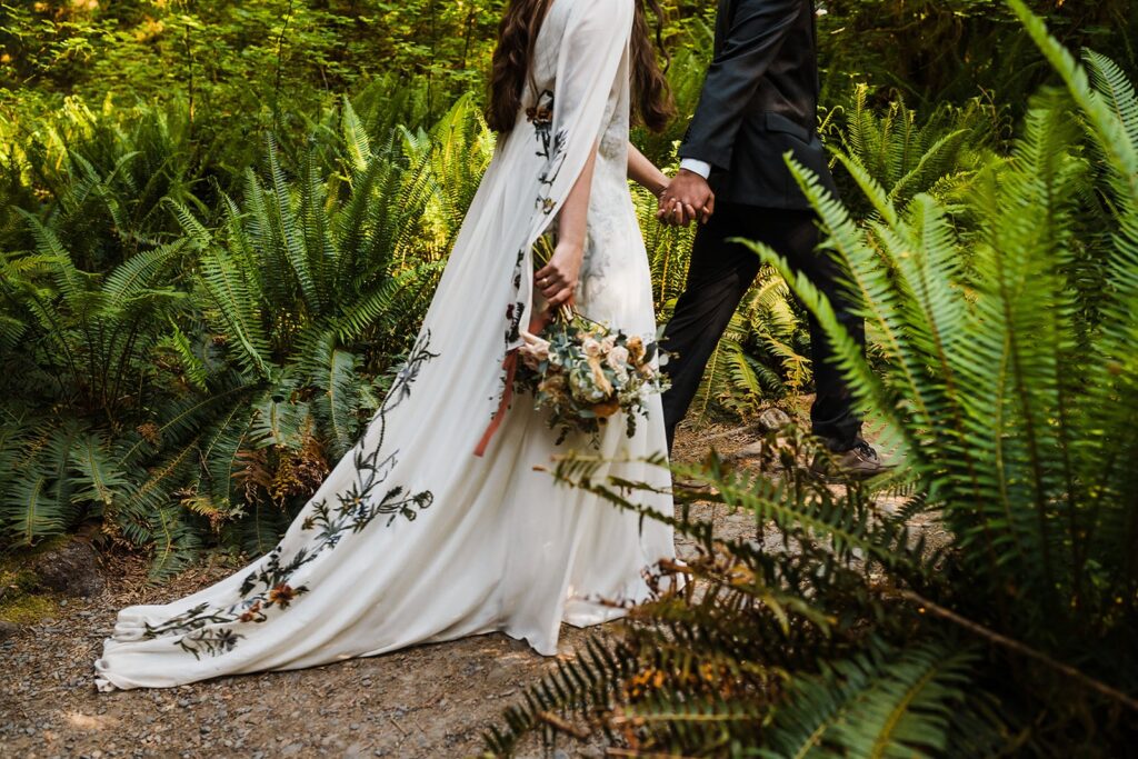 Bride and groom hold hands while walking through the Hoh Rainforest
