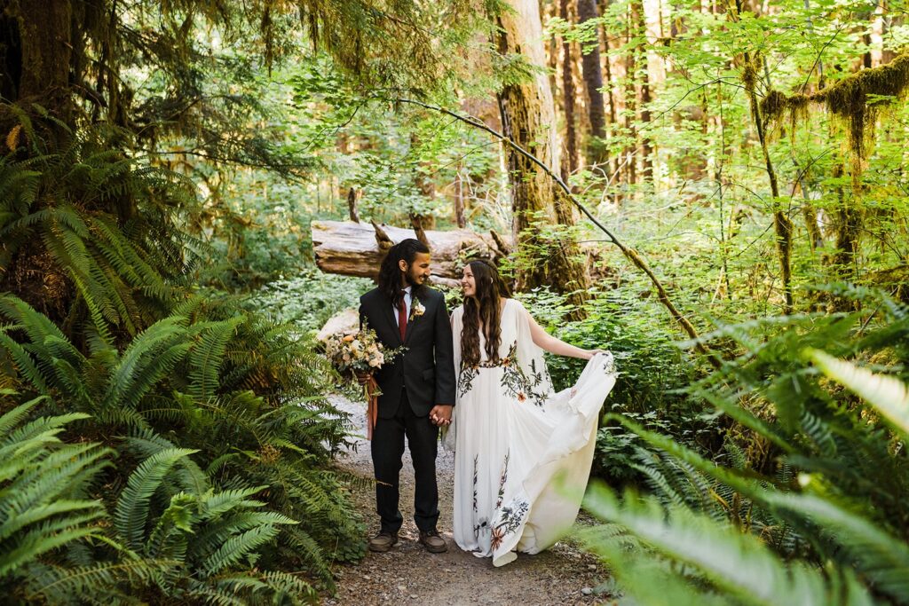 Bride and groom hold hands while walking through the forest during their Hoh Rainforest wedding