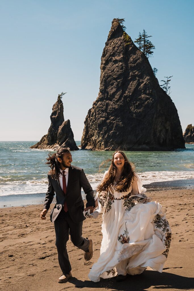 Bride and groom hold hands while running across the beach during their Hoh Rainforest wedding photos