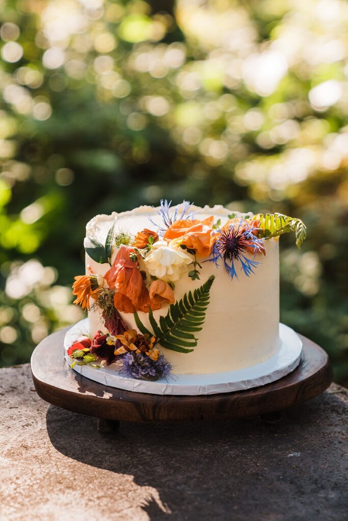 White frosted wedding cake with colorful flowers cascading over the edge
