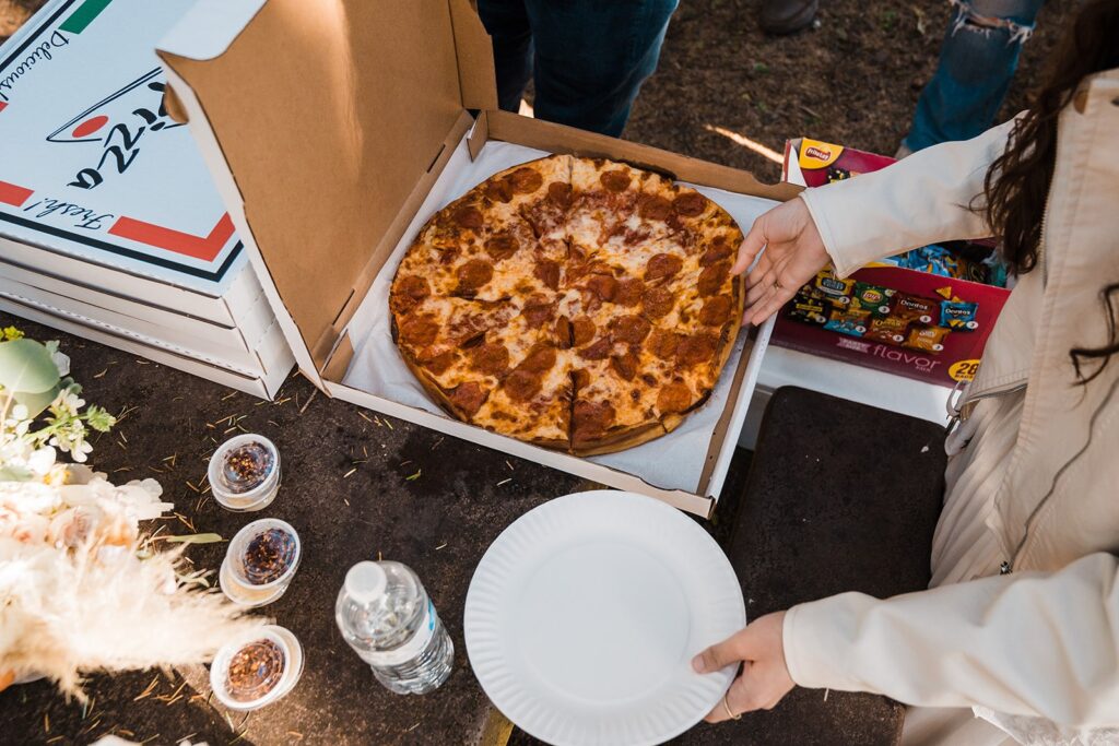 Bride reaching for a slice of pizza during their Hoh Rainforest wedding celebration picnic