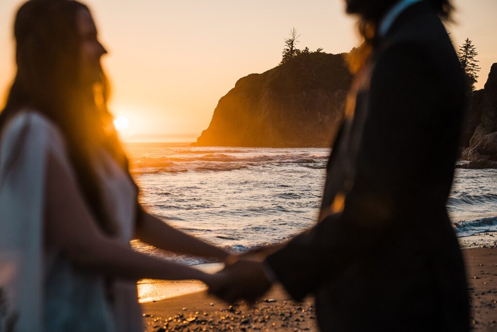 Bride and groom hold hands on the beach during their sunset Hoh Rainforest wedding photos