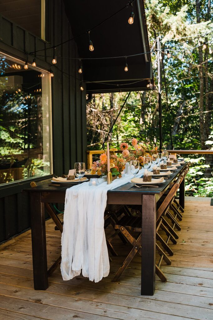 Outdoor Airbnb cabin wedding reception with white tablecloth and peach and orange flowers