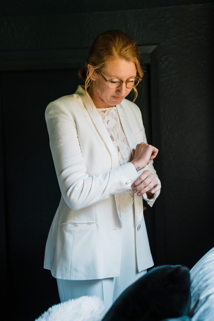 Bride adjusting cuff links on her white suit while getting ready for her wedding in Olympic National Park