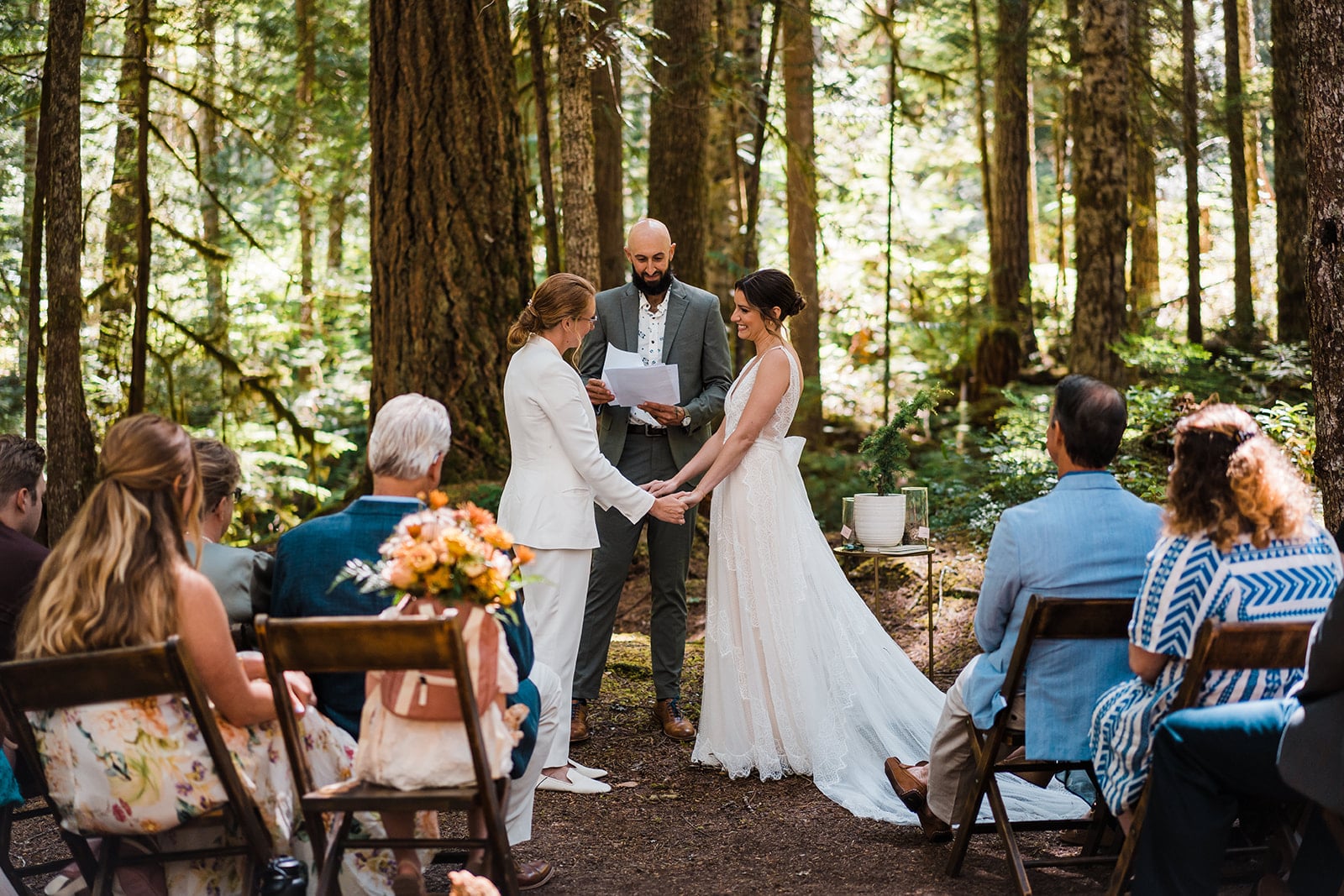 Brides hold hands during their micro wedding ceremony in the forest 