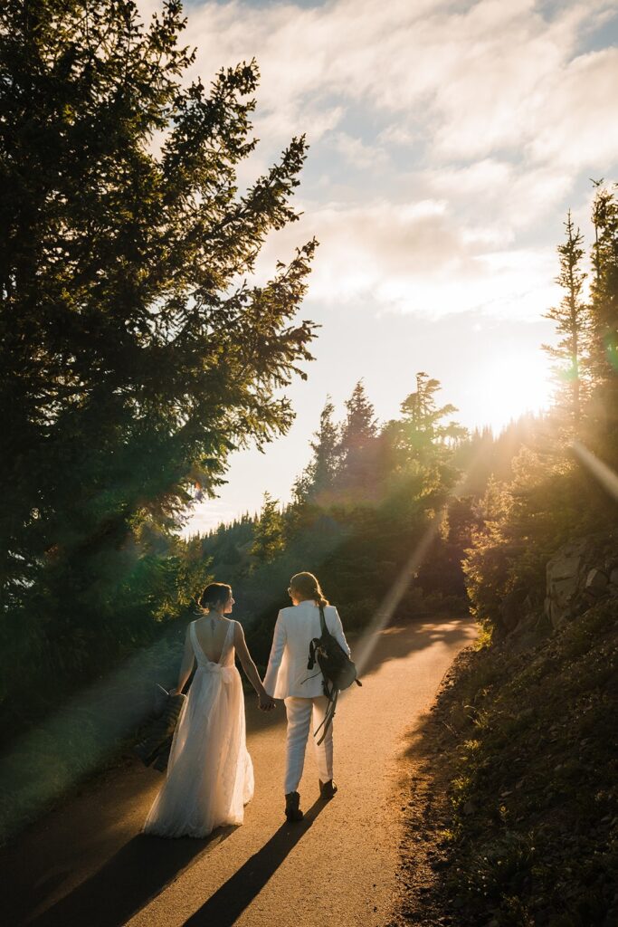 Brides hold hands and walk down a trail during sunset in Olympic National Park