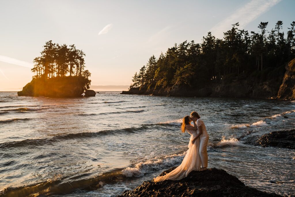 Brides kiss while standing on a rock surrounded by waves at their Olympic National Park wedding photos