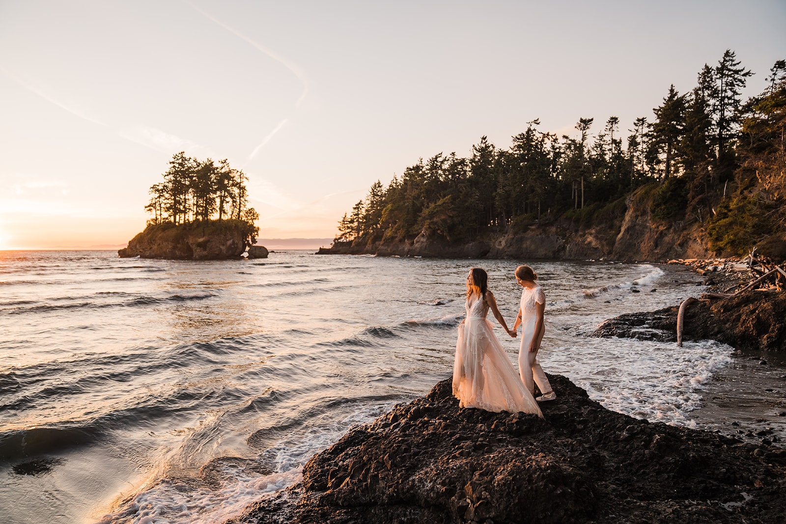 Two brides hold hands as they walk on a rocky shore during their elopement at a national park