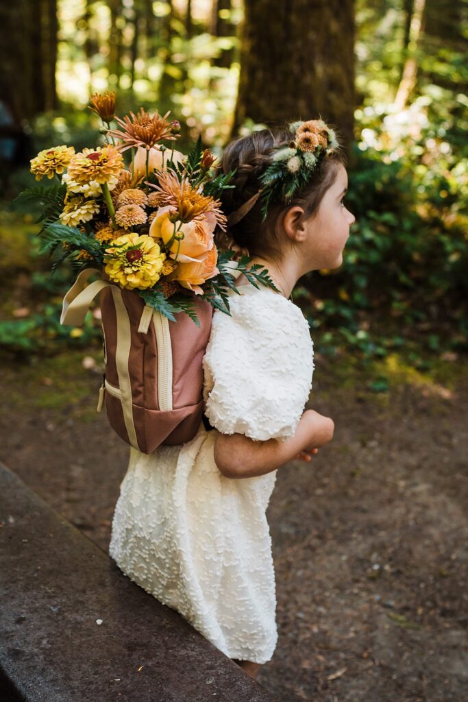 Flower girl wearing a white dress, flower crown and flower backpack for outdoor wedding ceremony in Olympic National Park