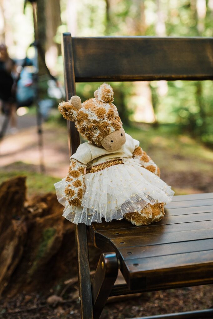 Stuffed giraffe in white dress sitting on a wood chair