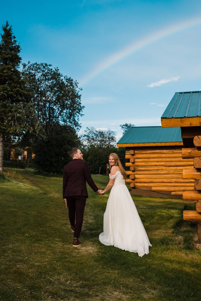 Bride and groom hold hands while walking away from their elopement cabin in Alaska