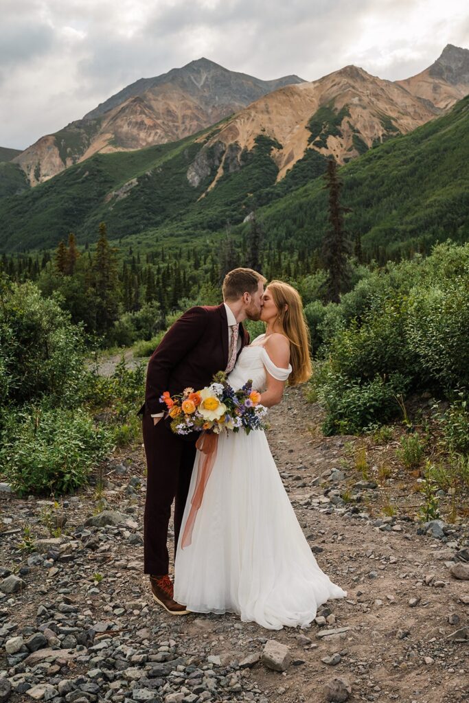 Bride and groom kiss at the base of the mountains in Alaska
