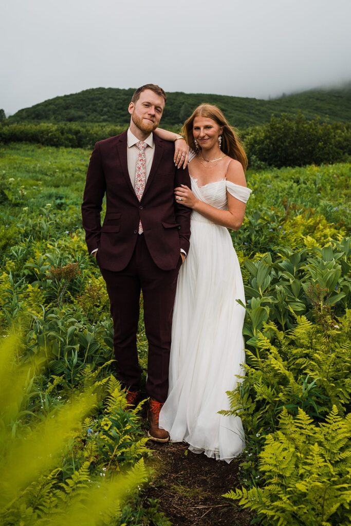 Bride and groom stand surrounded by lush greenery during their Alaska elopement
