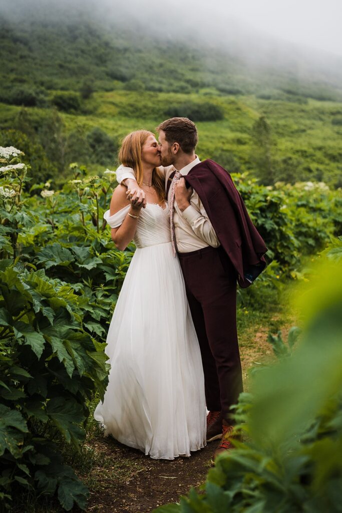Bride and groom kiss while surrounded by greenery at their Alaska elopement