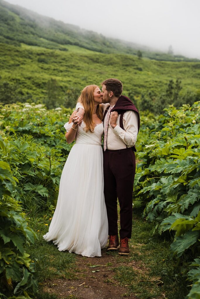 Bride and groom kiss surrounded by lush greenery during their elopement in Alaska