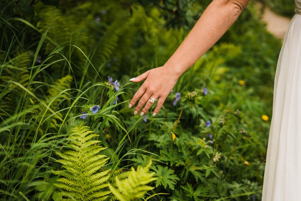 Bride trails her hands along the lush greenery on a hiking trail during her elopement in Alaska