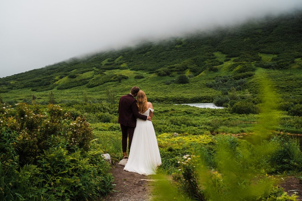 Bride and groom stand side by side looking out at the lush green mountains during their elopement in Alaska