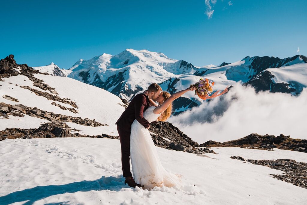 Bride and groom kiss while standing on the snow-covered mountains during their helicopter elopement in Alaska