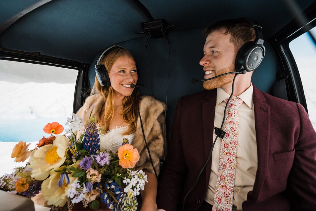 Bride and groom smile at each other while riding in a helicopter during their two-day elopement in Alaska