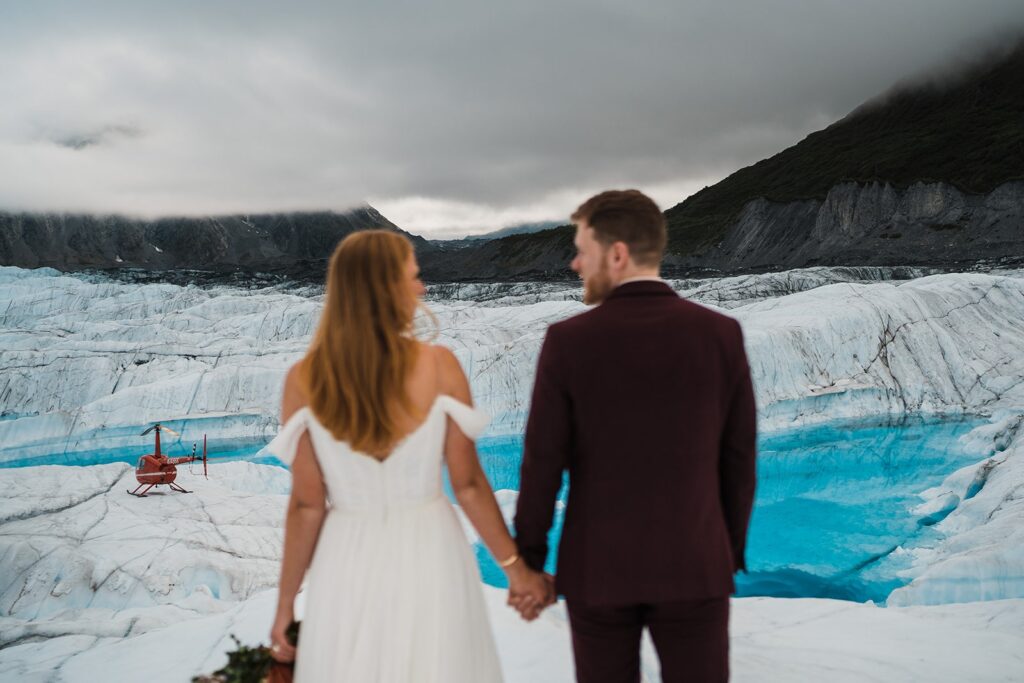 Bride and groom hold hands during their helicopter elopement photos in Alaska