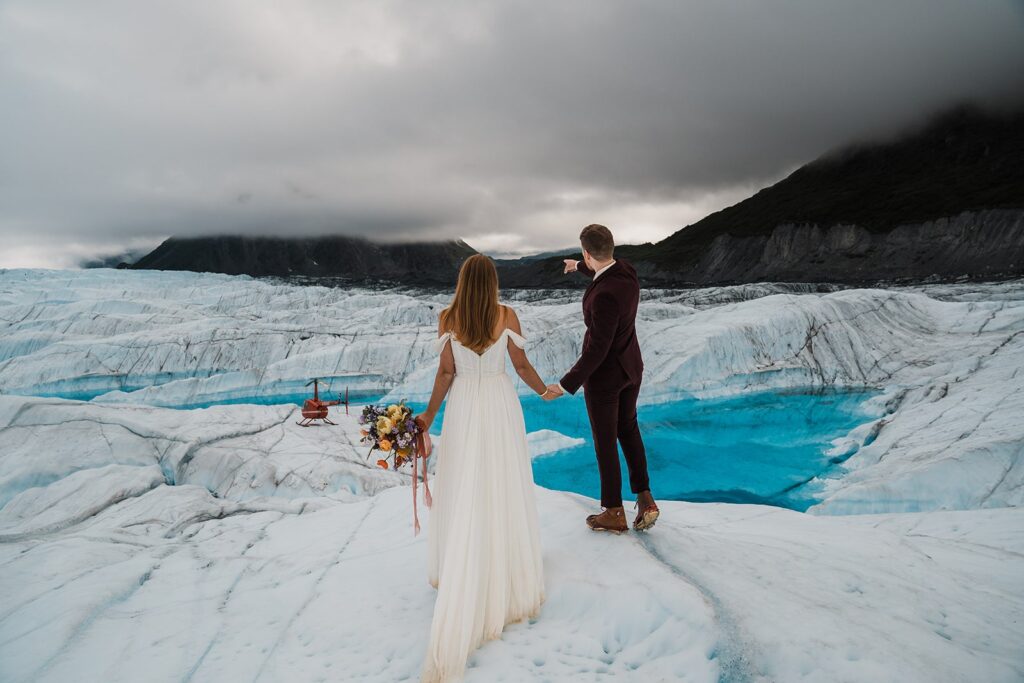 Groom points out over icy glacier during Alaska elopement 