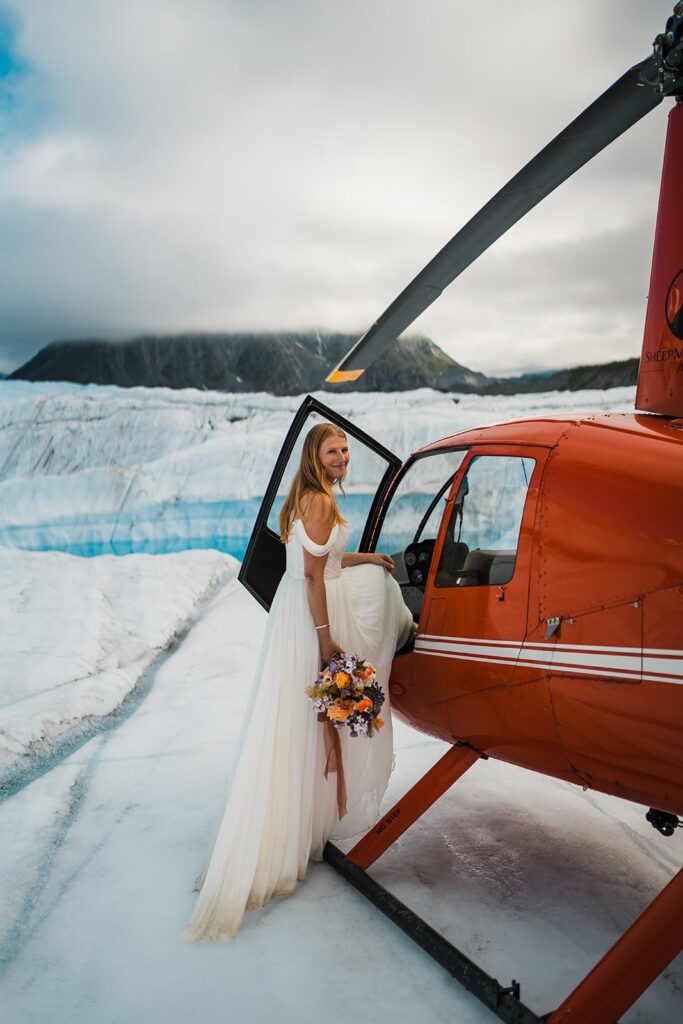 Bride steps into red helicopter after exploring a glacier during her elopement in Alaska