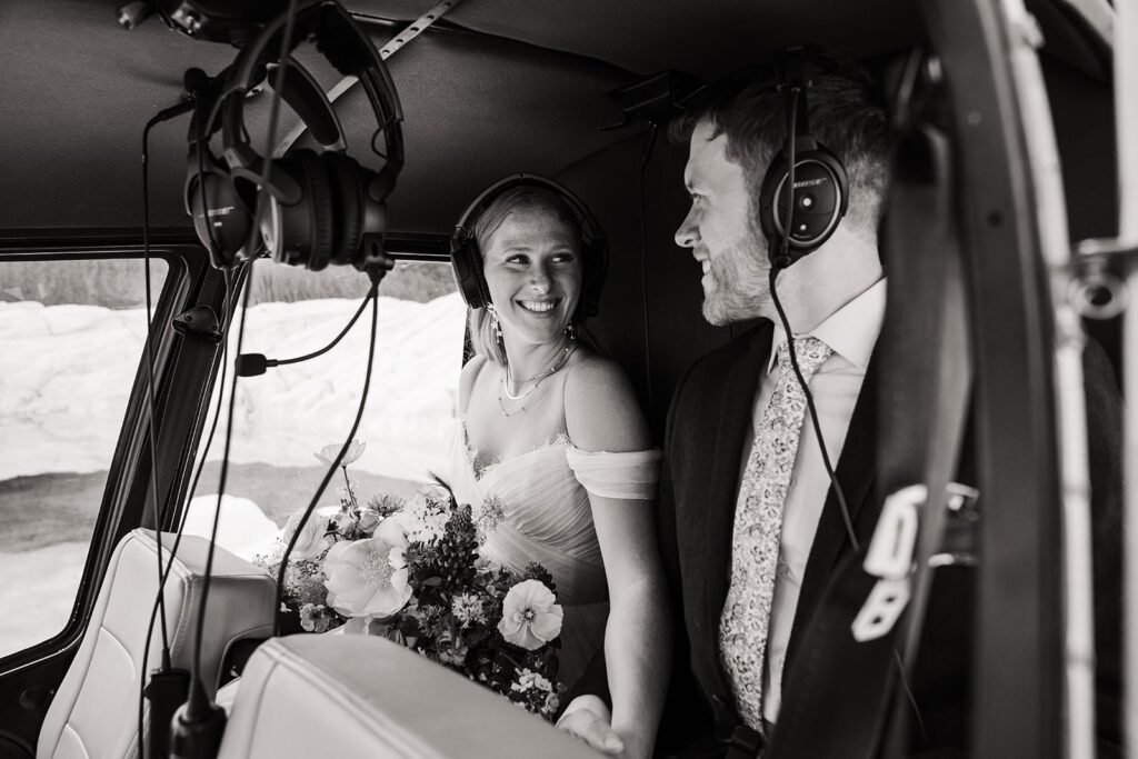 Bride and groom smile at each other while flying in a helicopter during their two-day elopement in Alaska