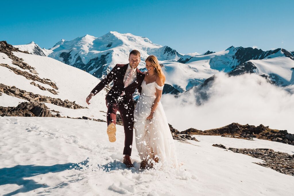 Groom kicks snow during helicopter elopement on a mountaintop in Alaska