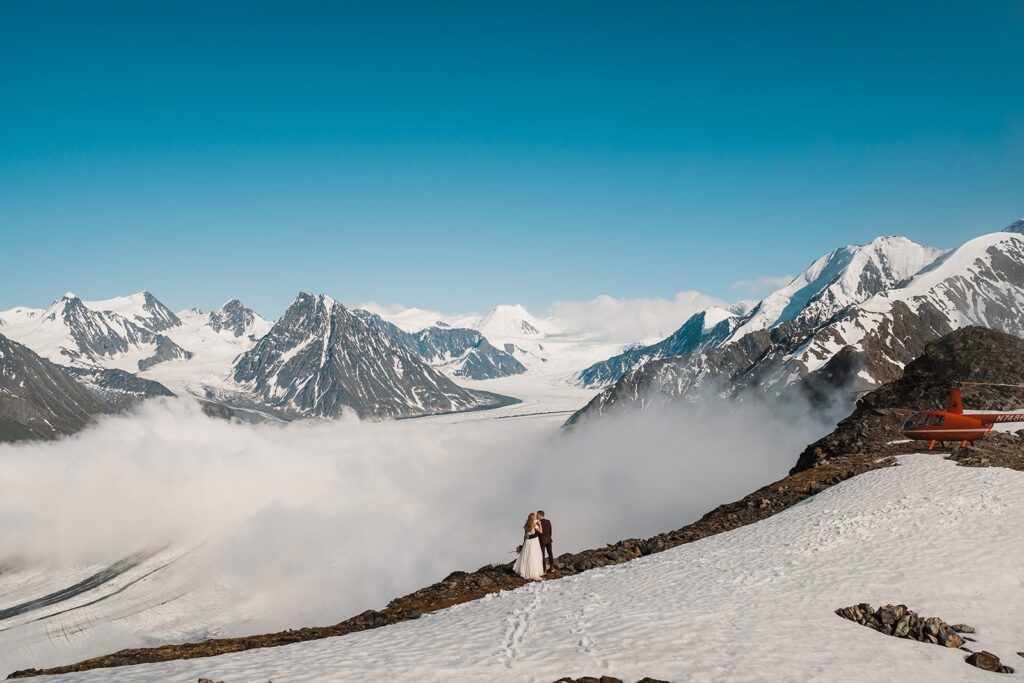 Bride and groom kiss during helicopter elopement on a mountaintop in Alaska