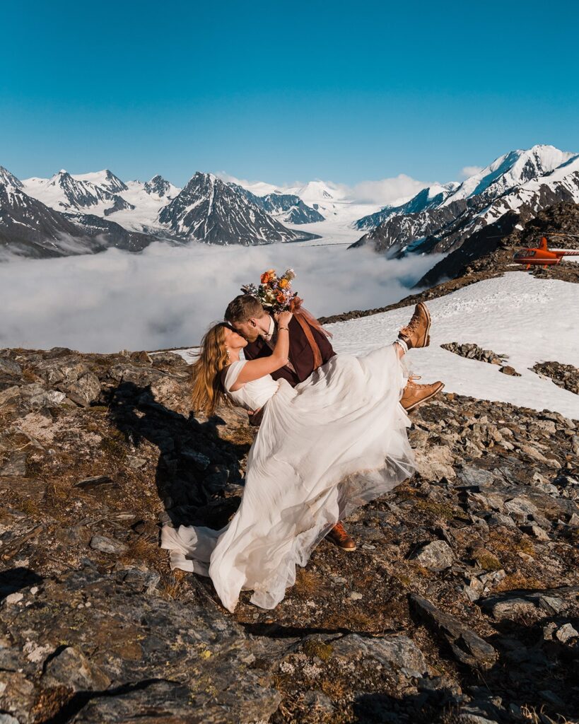 Groom dips bride back for a kiss during helicopter elopement on an Alaskan mountaintop