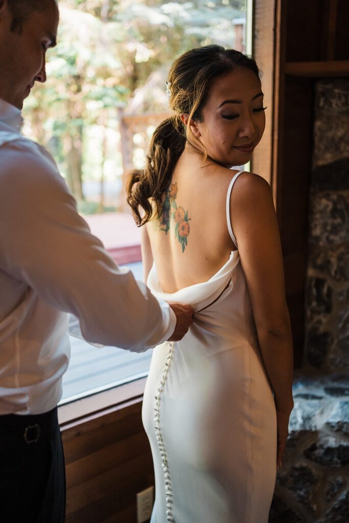 Groom helps zip bride into dress while getting ready for Artist Point elopement