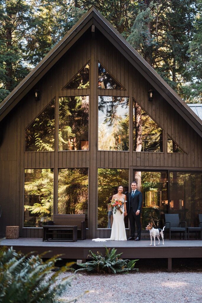 Bride and groom stand in front of Airbnb cabin with their dog during their Artist Point elopement
